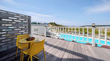 A wooden deck with a pool, yellow chairs, and a white fence.