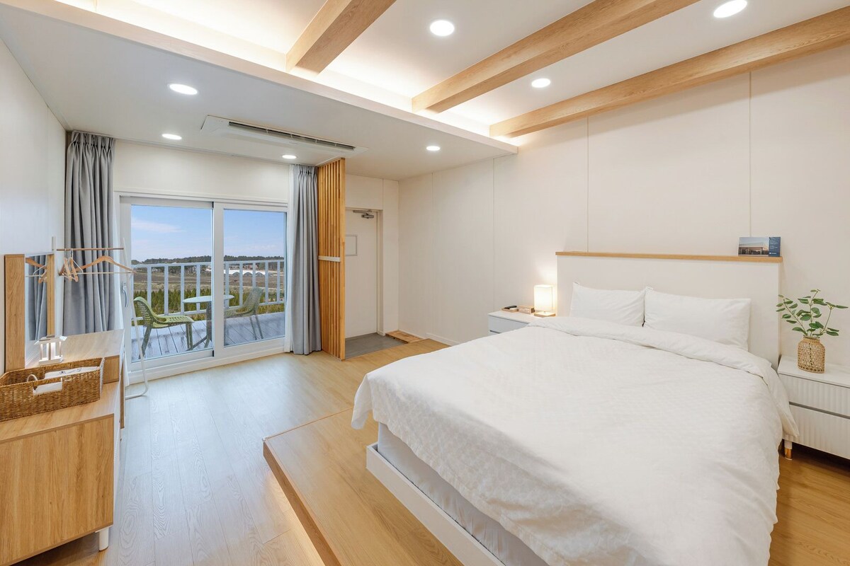 Une chambre d’hôtel dotée d’un grand lit, d’une table de chevet, d’une commode, d’un balcon avec vue et d’un plafond avec des poutres en bois et des spots encastrés.
