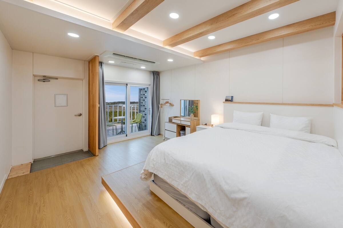 A modern hotel room with a large bed, a desk, and a sliding glass door leading to a balcony.