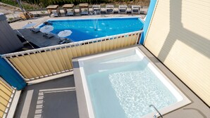 Een zwembad op het dak met een jacuzzi, ligbedden en parasols.