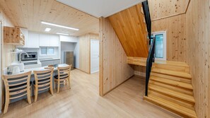 Cocina compacta con electrodomésticos modernos, comedor con sillas de madera y una escalera que sube a un nivel superior.