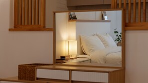Een slaapkamer met een bed, een bedlampje en een spiegel die de kamer weerspiegelt.