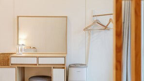 Habitación de hotel con tocador de madera, espejo, perchero, cesto de basura y ventana con cortinas.