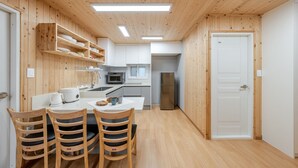 Eine kleine Küche mit Holzwänden, einem Esstisch mit Stühlen, einem Kühlschrank und einer Mikrowelle.