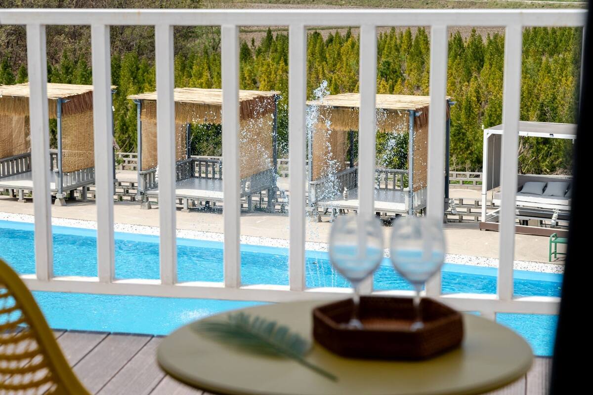 A poolside view with a thatched-roof structure, lounge chairs, and a table with a feather decoration.