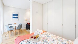 Una habitación de hotel moderna con una cama, una zona de comedor con sillas y una mesa, y un armario.