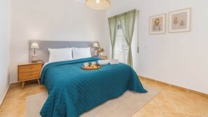 Un dormitorio con cama, mesitas de noche, lámpara, una bandeja con alimentos para el desayuno y cuadros en la pared.