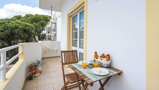 Un balcón con una mesa dispuesta para el desayuno, que incluye cruasanes y jugo de naranja, y una silla.