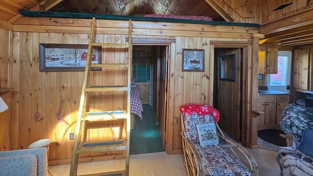 A wooden cabin interior with a loft bed, a ladder, a small table, and a sofa. - Idlewood Cabin 3 (Rangeley)