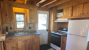 A kitchen with wooden cabinets, a stove, a microwave, and a refrigerator. - Idlewood Cabin 3 (Rangeley)