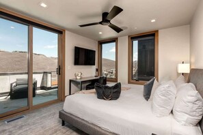 A hotel room with a bed, a desk, a chair, a ceiling fan, and large windows with a view of the landscape. - Abode at Powder King, ski-in/ski-out, hot tub, fire pit, PCMR (Park City)