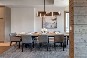 A modern dining area with a wooden table, six chairs, a hanging light fixture, and a large abstract painting on the wall. - Abode at Powder King, ski-in/ski-out, hot tub, fire pit, PCMR (Park City)