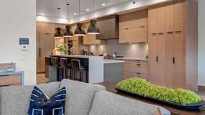 A modern kitchen with pendant lighting, a dining area with a sofa and a coffee table, and a small indoor garden.