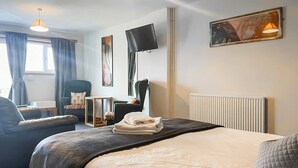 A hotel room with a bed, a chair, a desk, a TV, and a radiator. - 1 bedroom accommodation in Battle (Battle)