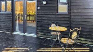 A building with a dark wooden exterior, a black door with a glass panel, and a small outdoor seating area with two chairs and a table. - 1 bedroom accommodation in Battle (Battle)