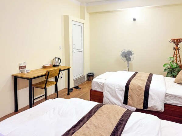 A hotel room with two beds, a desk, a chair, a fan, a plant, and a door. - Zen Nest Hotel (Kathmandu)