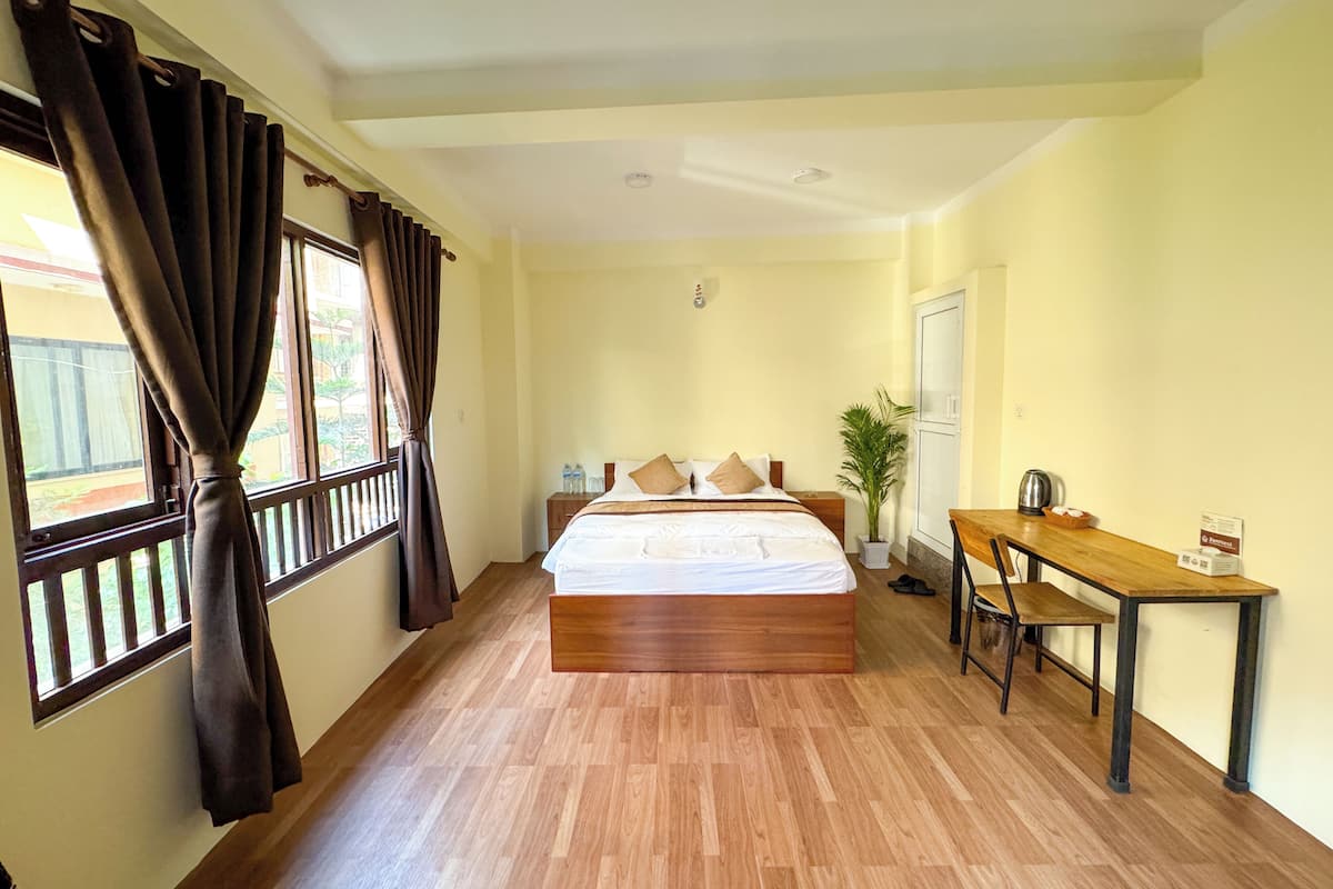 Una camera d'albergo con un letto grande, una scrivania, una sedia, una pianta in vaso e una finestra con tende.