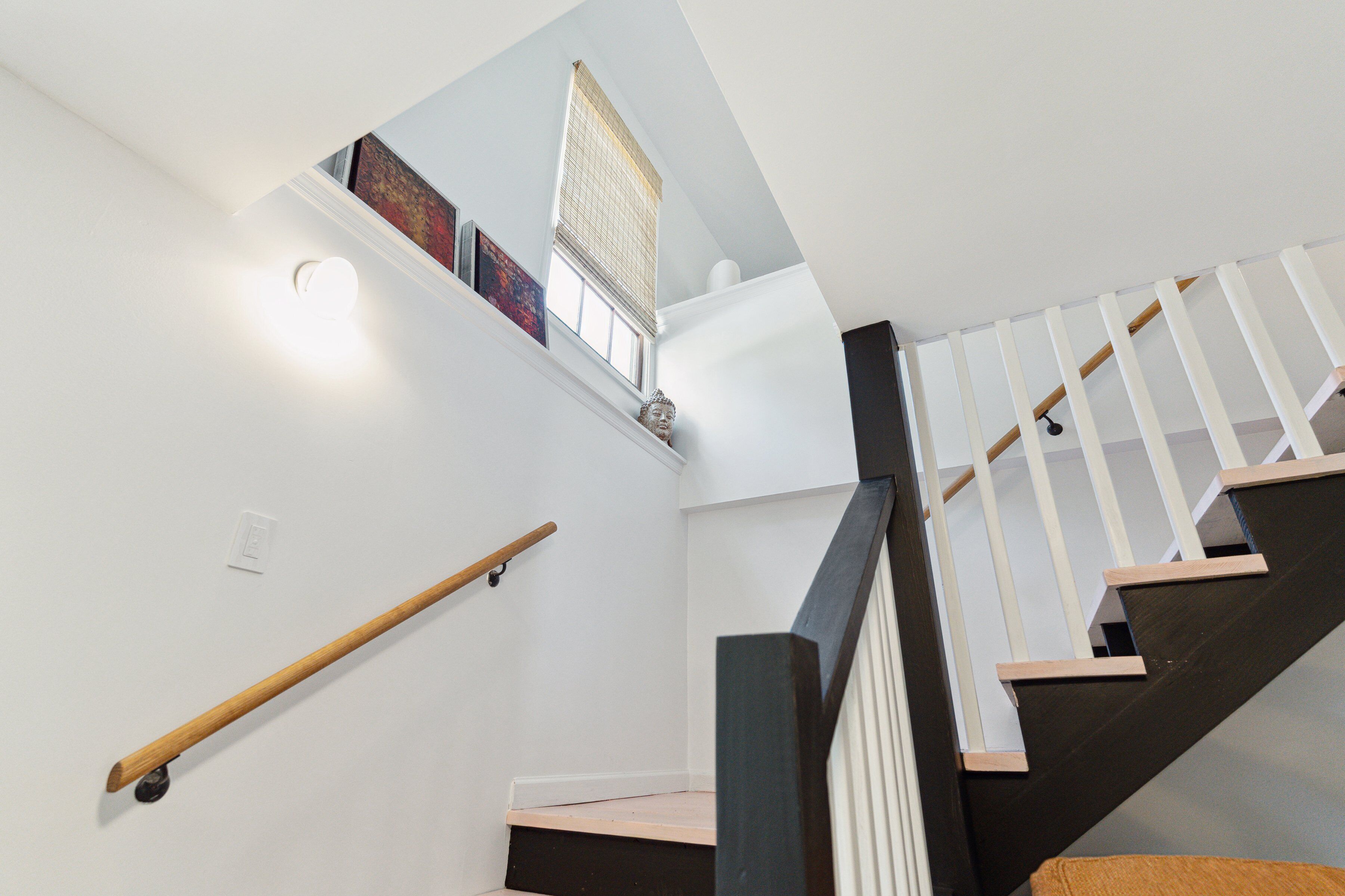 Eine Treppe mit Holzgeländer, einem schwarz-weißen Geländer und einem kleinen Fenster mit Außenblick.