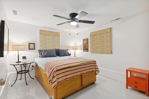 A bedroom with a bed, two bedside tables, a ceiling fan, and wall-mounted lamps.