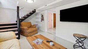 Una sala moderna con una escalera, un sofá, una mesa de centro con revistas y un televisor montado en la pared.