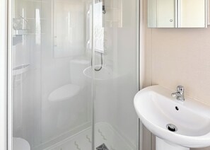 Une salle de bain moderne avec une douche à parois de verre, un lavabo blanc et un miroir au-dessus du lavabo.