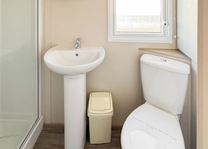 A bathroom with a white pedestal sink, a toilet, and a trash bin.