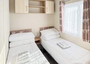 Une chambre de taille modeste, comprenant deux lits simples, une armoire en bois, une petite table et une fenêtre avec des rideaux.