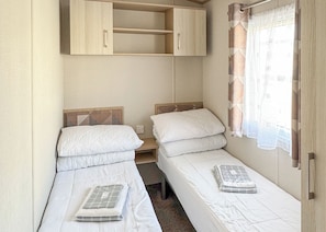 A compact room with two single beds, a wooden wardrobe, and a window with curtains.