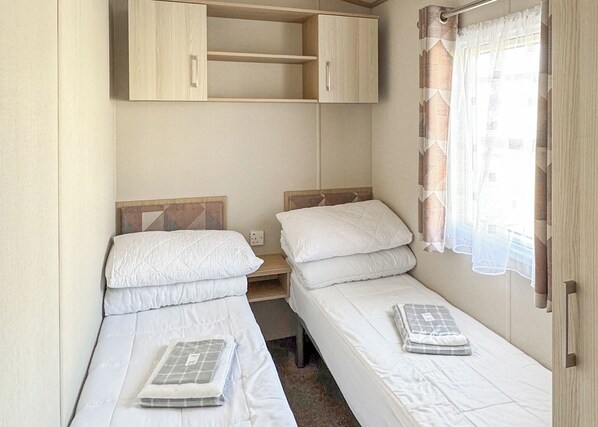 A compact room with two single beds, a wooden wardrobe, and a window with curtains.