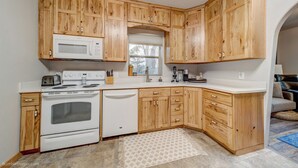 A kitchen with wooden cabinets, a white microwave, a stove, and a dishwasher. - Charming 2-bedroom bungalow in the heart of Coeur d'Alene with backyard oasis (Coeur d'Alene)
