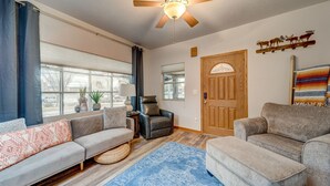 A living room with a ceiling fan, a sofa, an ottoman, a chair, and a wooden door. - Charming 2-bedroom bungalow in the heart of Coeur d'Alene with backyard oasis (Coeur d'Alene)