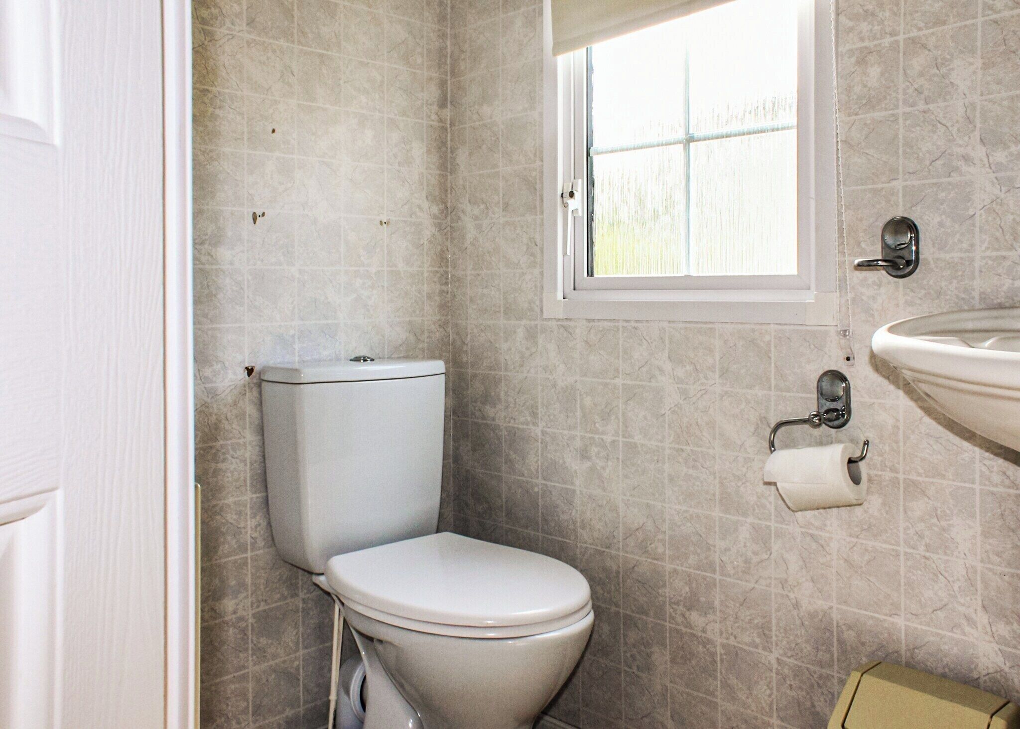 A small bathroom with a toilet, a window, and a sink.