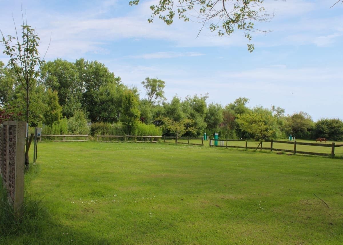 Ein grünes Feld mit Holzzaun, Bäumen und einem Picknicktisch im Hintergrund.