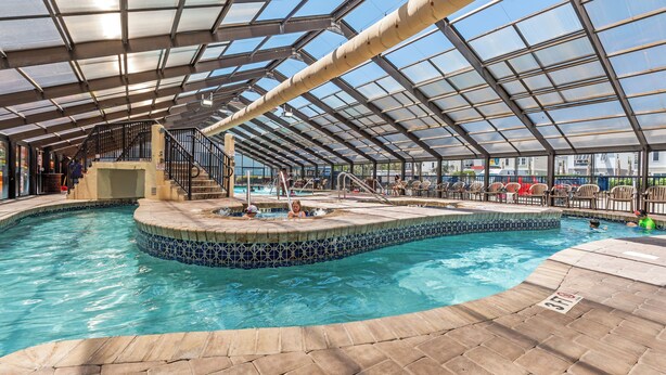 An indoor swimming pool with a glass ceiling, tiled edges, and a stone floor. - Oceanview Vibes! Compass Cove Studio Retreat (Myrtle Beach)