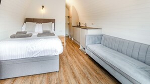 A bedroom with a bed, a gray sofa, wooden flooring, and a white ceiling. - Lakeside Micro Lodge (Pet) (Scarborough)