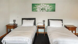 A hotel room with two single beds, a nightstand with a lamp, a painting of a flower on the wall, and a carpeted floor. - 1 bedroom accommodation in Battle (Battle)