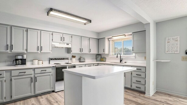A modern kitchen with white cabinets, a central island, a stove, and a window with blinds. - Little Sand Cottage 3-bedroom cottage with AC, WiFi in serene Grant (Grant)