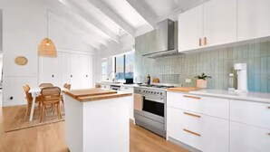 Une cuisine moderne avec des meubles blancs, un îlot central et un coin repas comprenant des chaises et une table en bois.