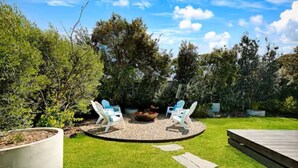 Un espace de détente circulaire comprenant deux chaises et un foyer, entouré d’un chemin de gravier et d’une terrasse en bois.