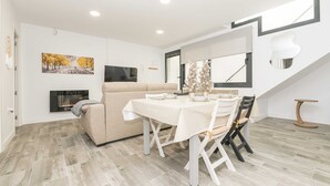 Un salon moderne avec un canapé, une table à manger et des chaises. On y trouve une cheminée, un tableau au mur et une fenêtre donnant sur un beau paysage.
