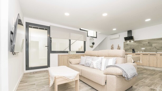 Un salon moderne avec un canapé beige, une table basse en bois et un escalier menant à l’étage supérieur.