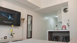 Une chambre d’hôtel moderne équipée d’un lit, d’un téléviseur fixé au mur, d’un miroir, d’un bureau avec deux tabourets et d’une horloge murale.