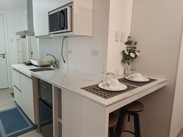 A compact kitchen with a microwave, sink, and bar stools.