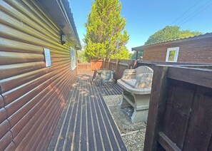 A wooden deck with a grill and seating area, a wooden fence, and a tall tree in the background. - Open plan lodge with two doubles, both with TV/DVD. (Brecon Beacons National Park,)
