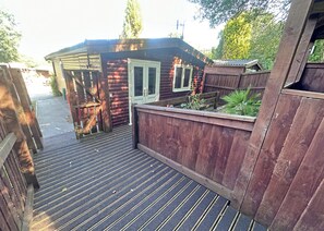 A wooden deck leading to a cabin with a door and windows, surrounded by a wooden fence and greenery. - Open plan lodge with two doubles, both with TV/DVD. (Brecon Beacons National Park,)