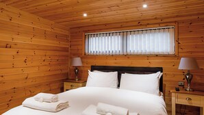 Una habitación con paneles de madera, una cama, dos mesitas de noche y una ventana con persianas.