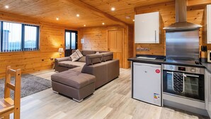 Interior acogedor de una cabaña con sofá, paredes de madera, una kitchenette y una ventana con vista a la ciudad.