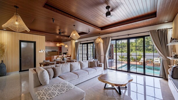 A spacious living room with a large sofa, a coffee table, and a dining area with a kitchen in the background. - The Lotus Villa Uluwatu (Ungasan)