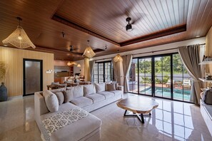 A spacious living room with a large sofa, a coffee table, and a dining area with a kitchen in the background. - The Lotus Villa Uluwatu (Ungasan)