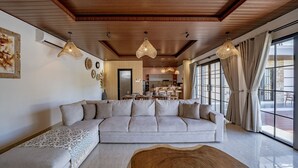 A modern living room with a sectional sofa, a wooden coffee table, and pendant lighting. - The Lotus Villa Uluwatu (Ungasan)